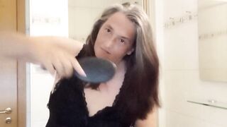 Aged woman with real silver strands lazily combs her lengthy hair